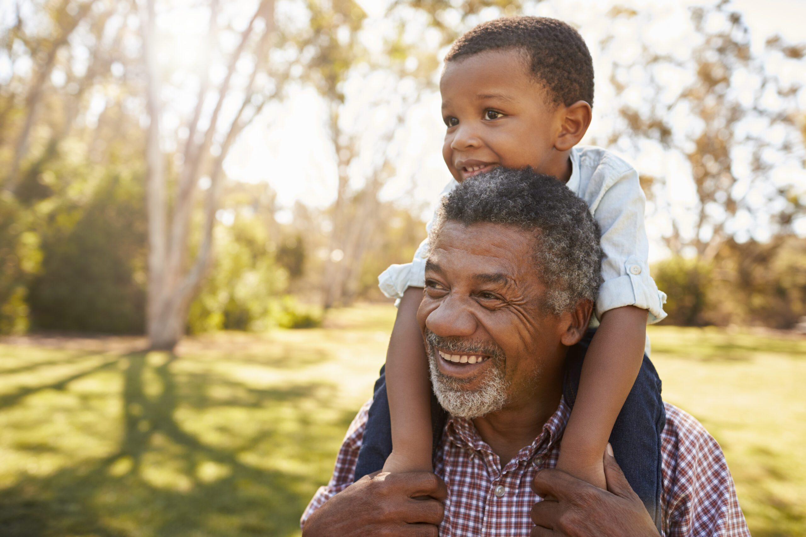 A grandfather carries his grandson on his shoulders in the park