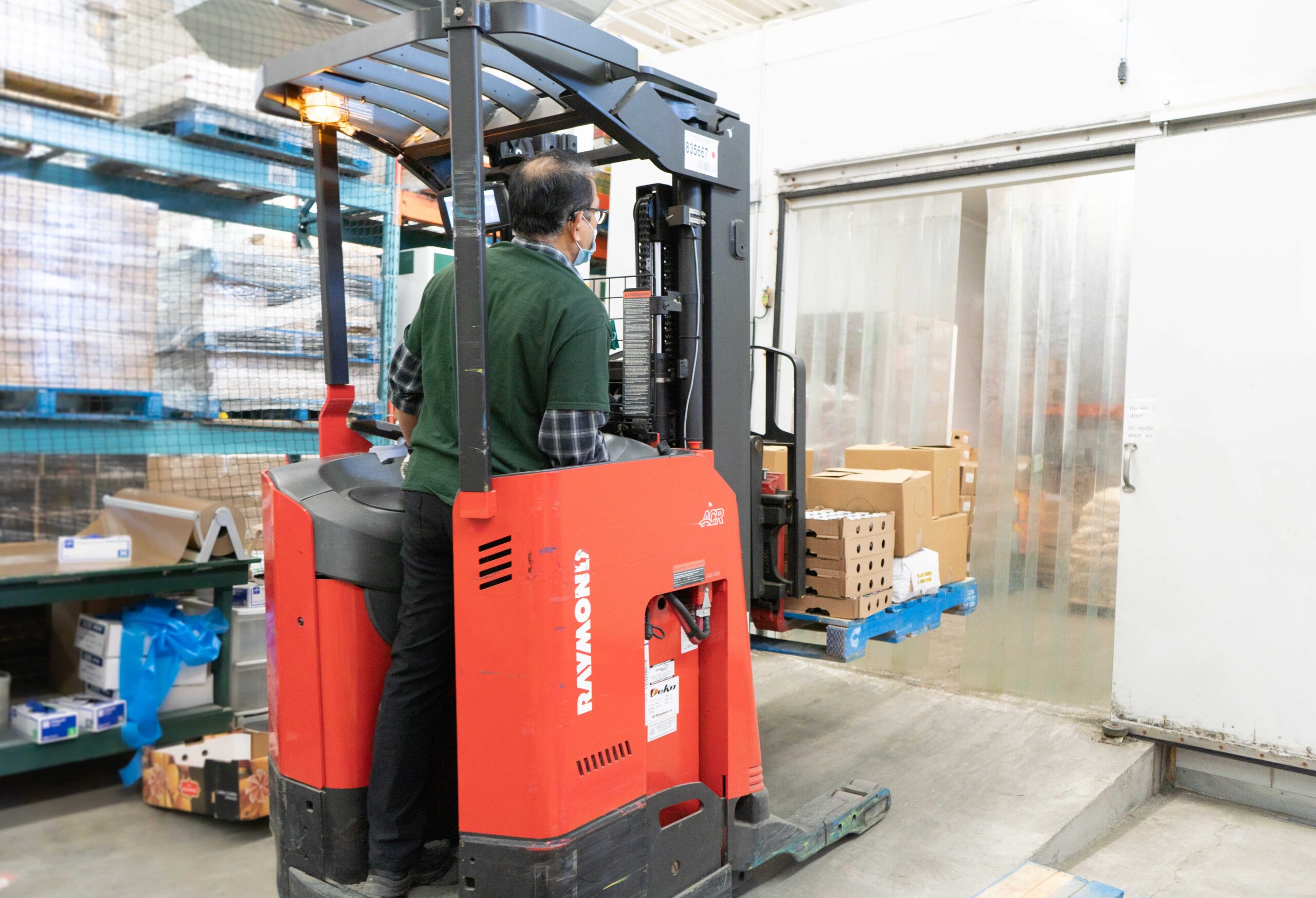 The Mississsauga Food Bank staff member operating a forklift in the warehouse to move a skid of food into the refridgerator.