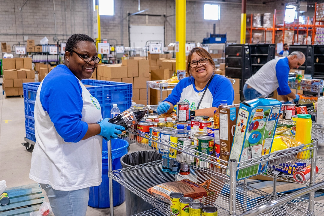 Volunteers in warehouse standing near full shelves of food