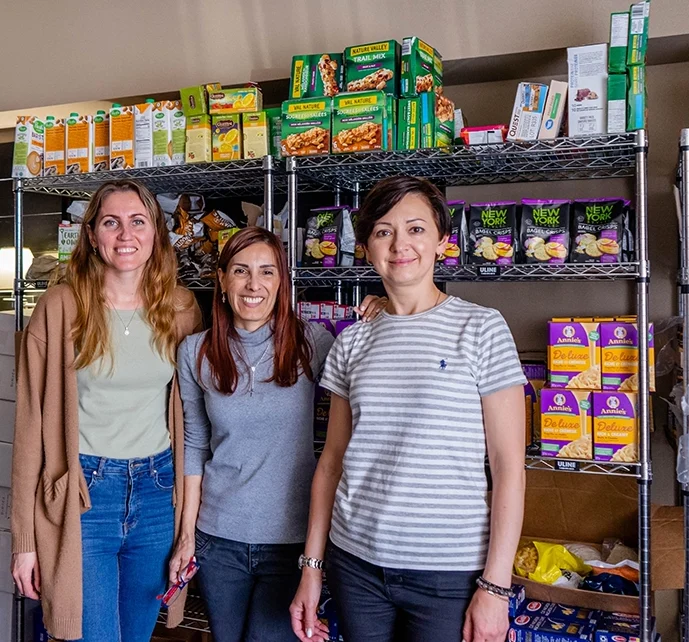 Volunteers stand in front of shelves of food at food pantry