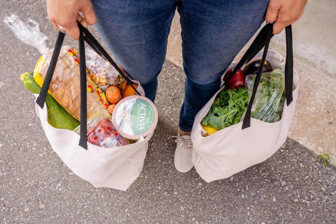 Person holding 2 full tote bags of food