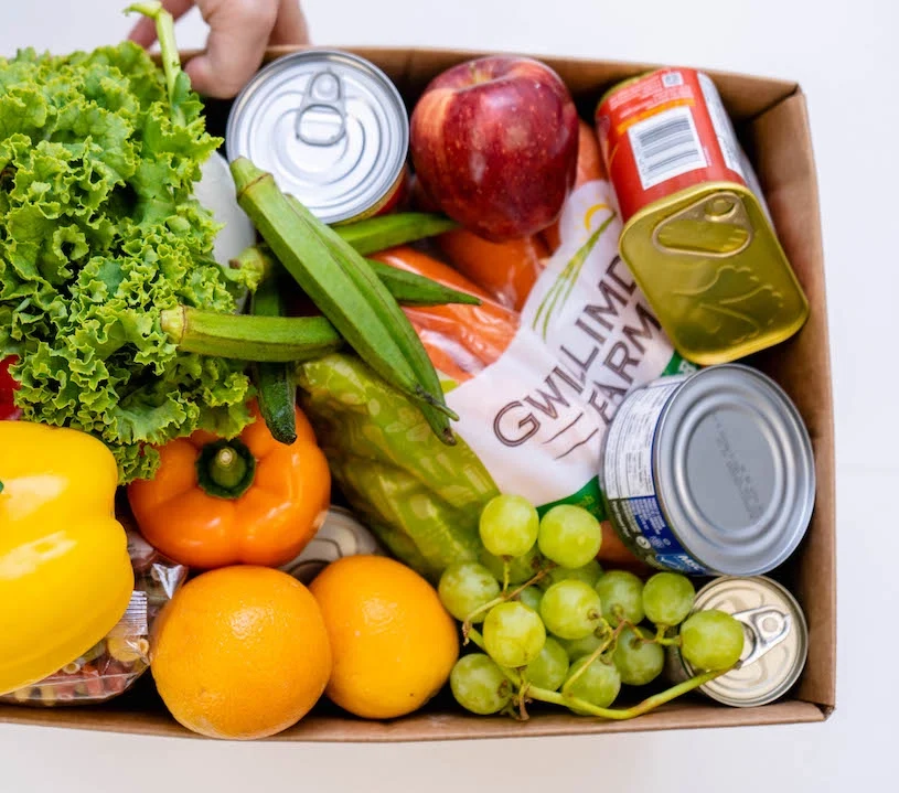 View of open box of food with fresh food and canned goods