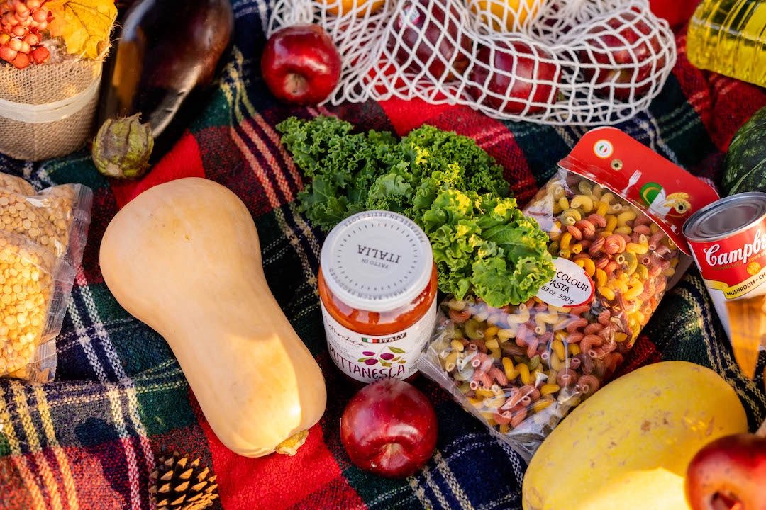 Table covered by picnic blanket, holding fall and winter vegetables, jars and cans