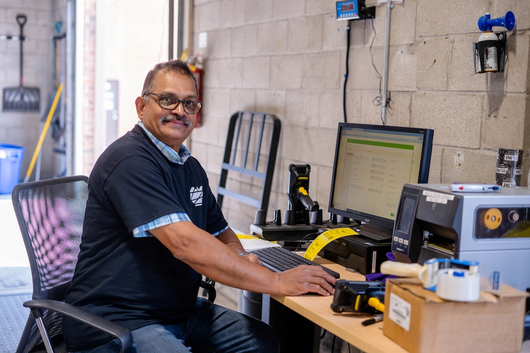 Warehouse team member smiling and sitting at computer