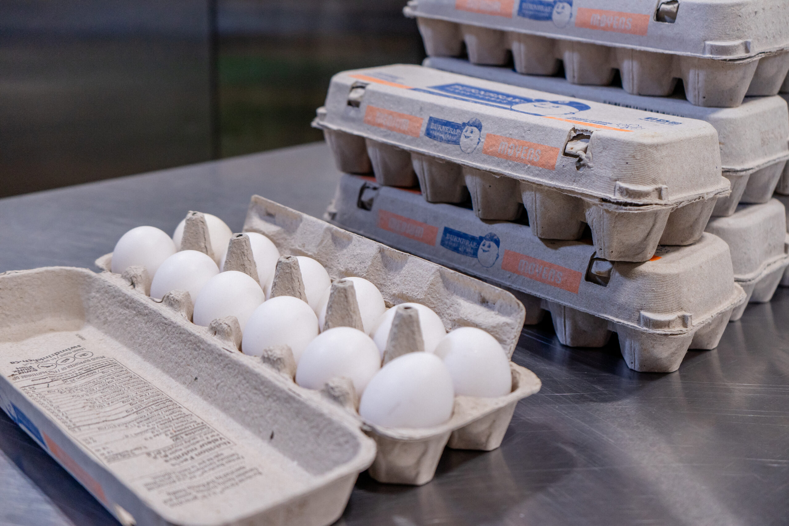Cartons of eggs stacked on a metal table with one carton open to show eggs inside.