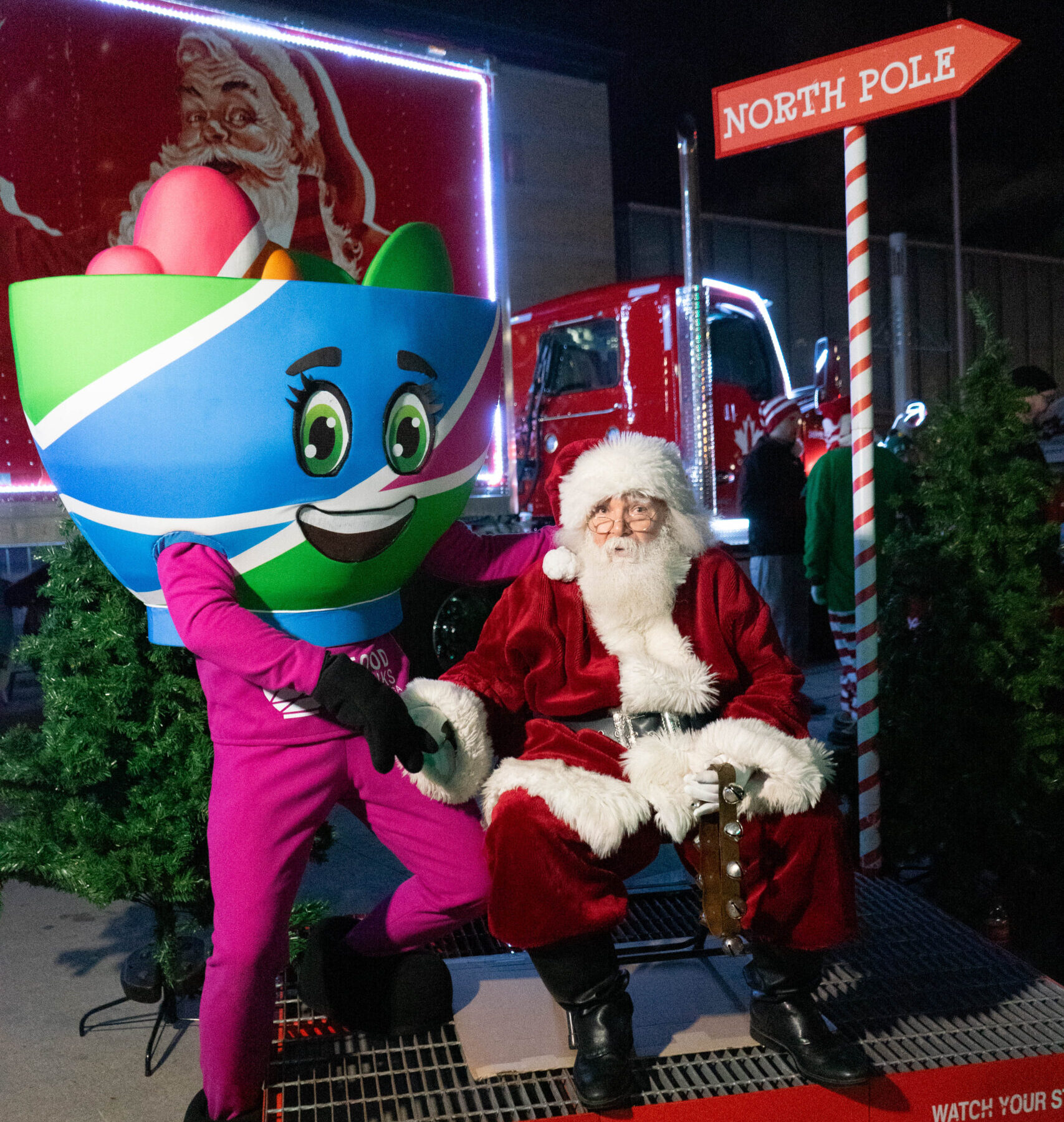 Food Banks Mississauga mascot, Bowlina, shaking hands with Santa Claus in front of a candy cane striped North Pole sign.