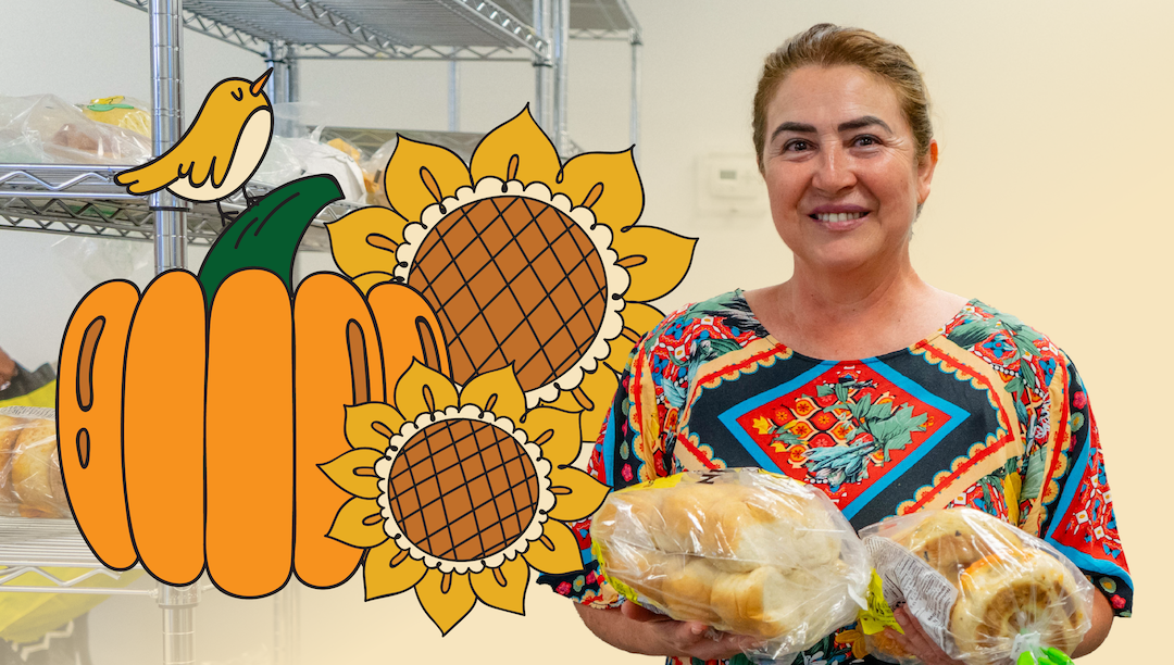 Food bank visitor in a colourful top holding two bags of fresh bread with illustrations of a pumpkin, two sunflowers and a small yellow bird to the left of her.